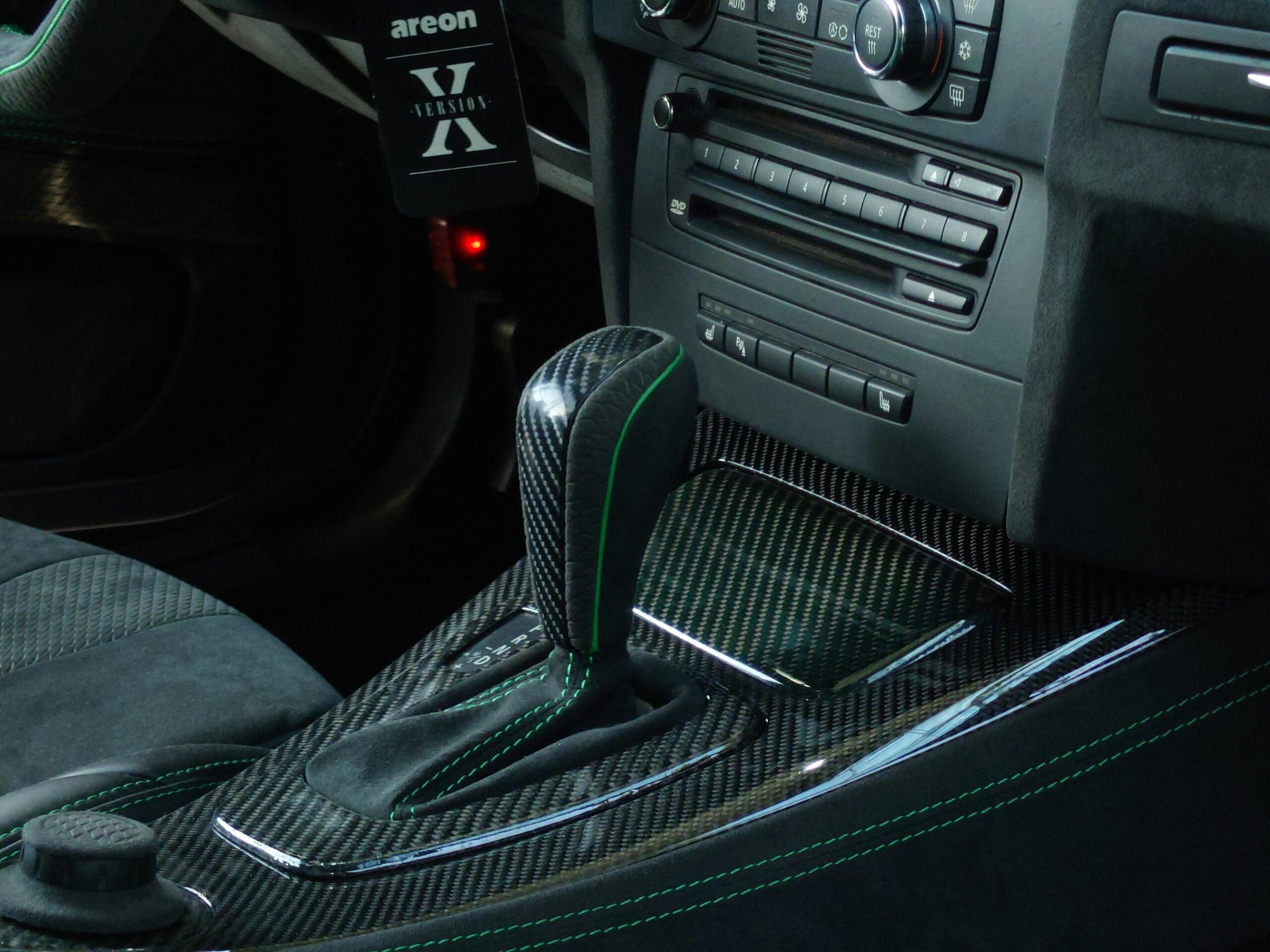 Close-up of a luxury car's interior featuring carbon fiber detailing, automatic gear shifter, and modern controls.