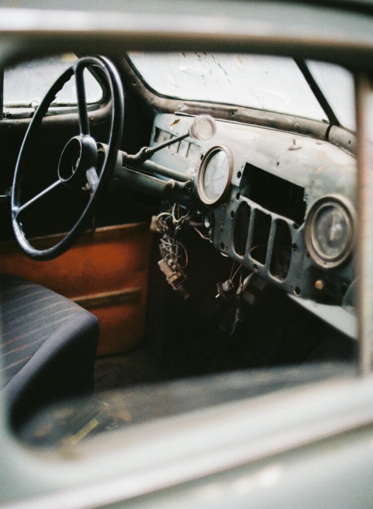 Interior of vintage automobile with steering wheel and speedometer with arrow on rusty surface near wire bundle in daylight