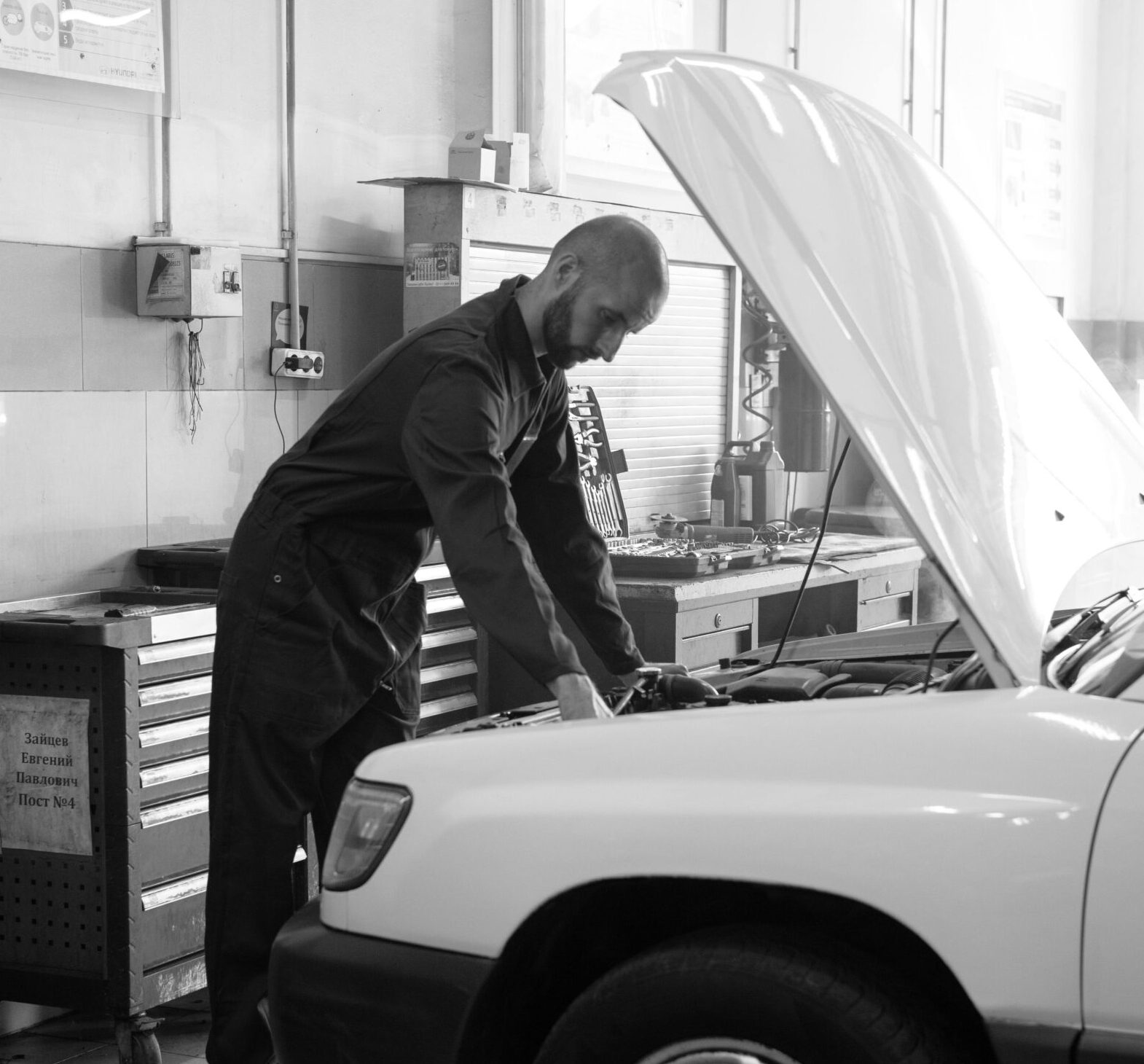 Mechanic in coverall inspecting a car engine inside a well-lit workshop.