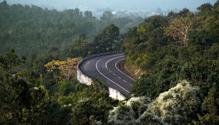 A scenic winding road through dense green forest in Ranchi, India, with vibrant foliage.